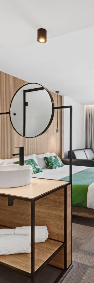 Habitaci&oacute;n moderna con cama, lavabo y espejo redondo en el centro.